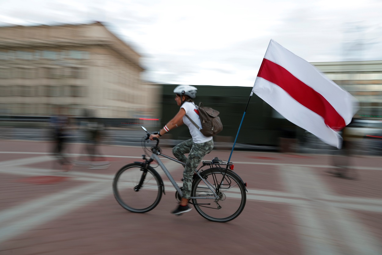 Una mujer en bicicleta lleva la histórica bandera presoviética de Bielorrusia, durante las manifestaciones contra los resultados de las elecciones presidenciales, que dieron la victoria a Aleksandr Lukashenko, en Minsk. REUTERS/Vasily Fedosenko