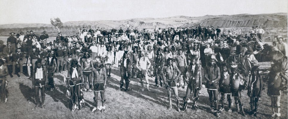 Braves: A portrait of a band of Big Foots (Miniconjou) in an open field, at a Grass Dance on the Cheyenne River, watched by soldiers from the 8th U.S. Cavalry and 3rd Infantry