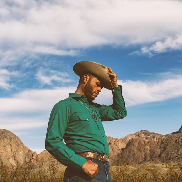 Texas Honky-Tonker Charley Crockett tips his hat with a scenic West Texas in the background.