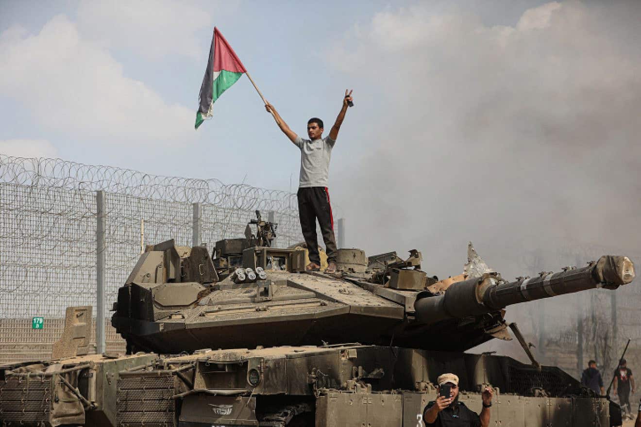 Palestinians stand next to a burning tank inside the border fence with Israel near the city of Khan Yunis in the southern Gaza Strip. October 7, 2023. Photo by Yousef Mohammed/FLASH90.