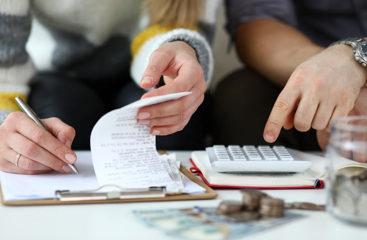 Close-up view of man and woman making account of family income. Writing down and calculating expenses. Attentive review of finance. Calculator on desk