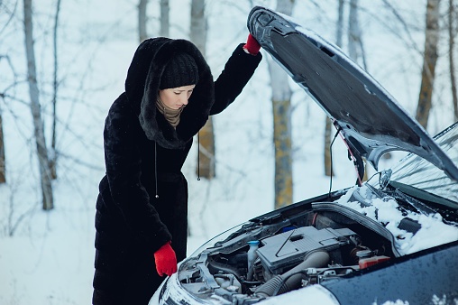 Woman checks under the hood of her car in snowy conditions.