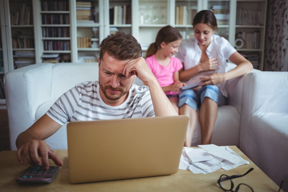 Worried man calculating bills while his wife and daughter sitting on sofa in living room