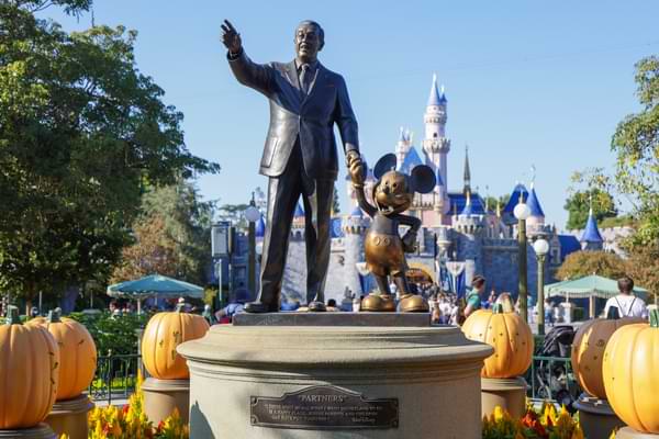 A statue of Walt Disney holding the hand of Mickey Mouse in front of the Disneyland castle in Anaheim, CA.