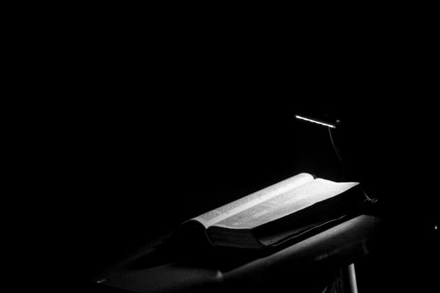 In a black-and-white image, an open Bible sits on a lectern, a single light shining down on it. © By Harry/stock.adobe.com