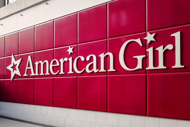 The American Girl logo in white on a tiled red background. © By JHVEPhoto/stock.adobe.com