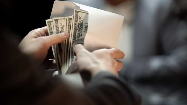 A person opens a white envelope filled with hundred-dollar bills. © By motortion/stock.adobe.com