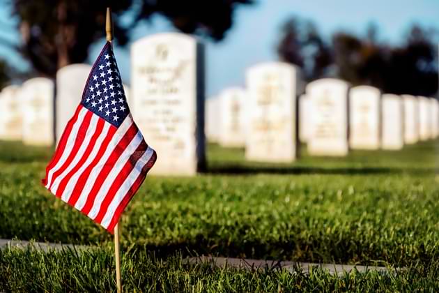 A lone American flag stands in front of multiple gravestones on Memorial Day. © By Bill Chizek/stock.adobe.com