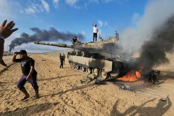 Palestinians celebrate by a destroyed Israeli tank at the Gaza Strip fence east of Khan Younis southern Saturday, Oct. 7, 2023. (AP Photo/Hassan Eslaiah)