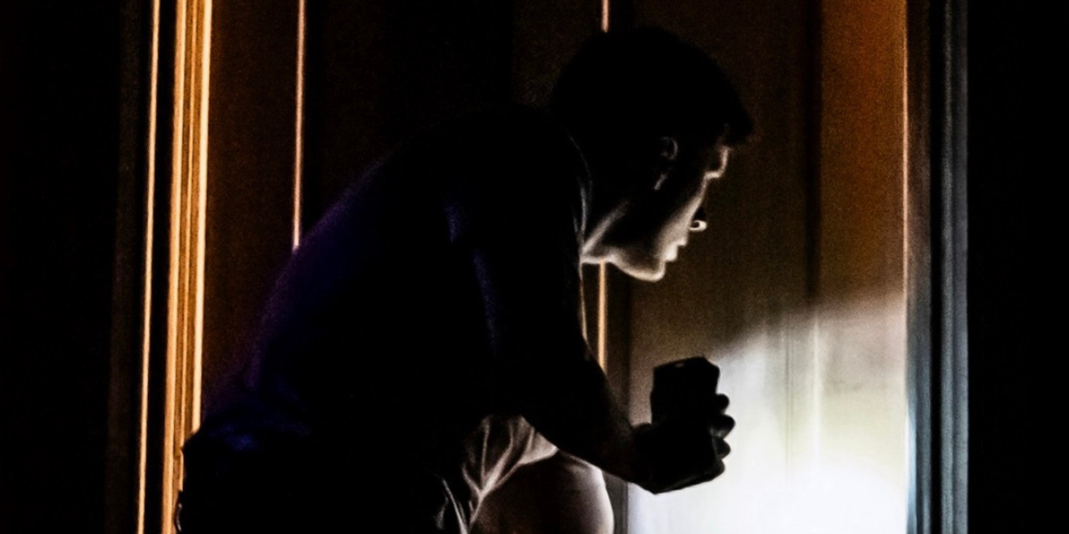 Silhouette of a person with a flashlight facing a door in the dark.