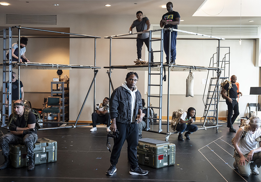 People in a rehearsal space with metal scaffolding structures, engaged in various activities.