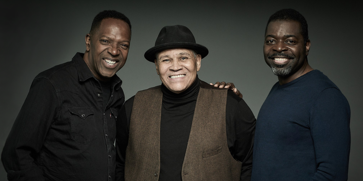 Three men smiling at the camera against a dark
background.
