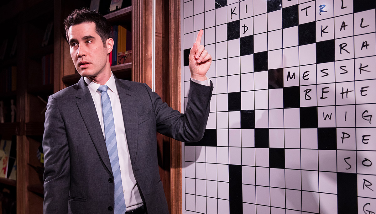 A man with dark hair wearing a suit stands in front of a large
crossword puzzle