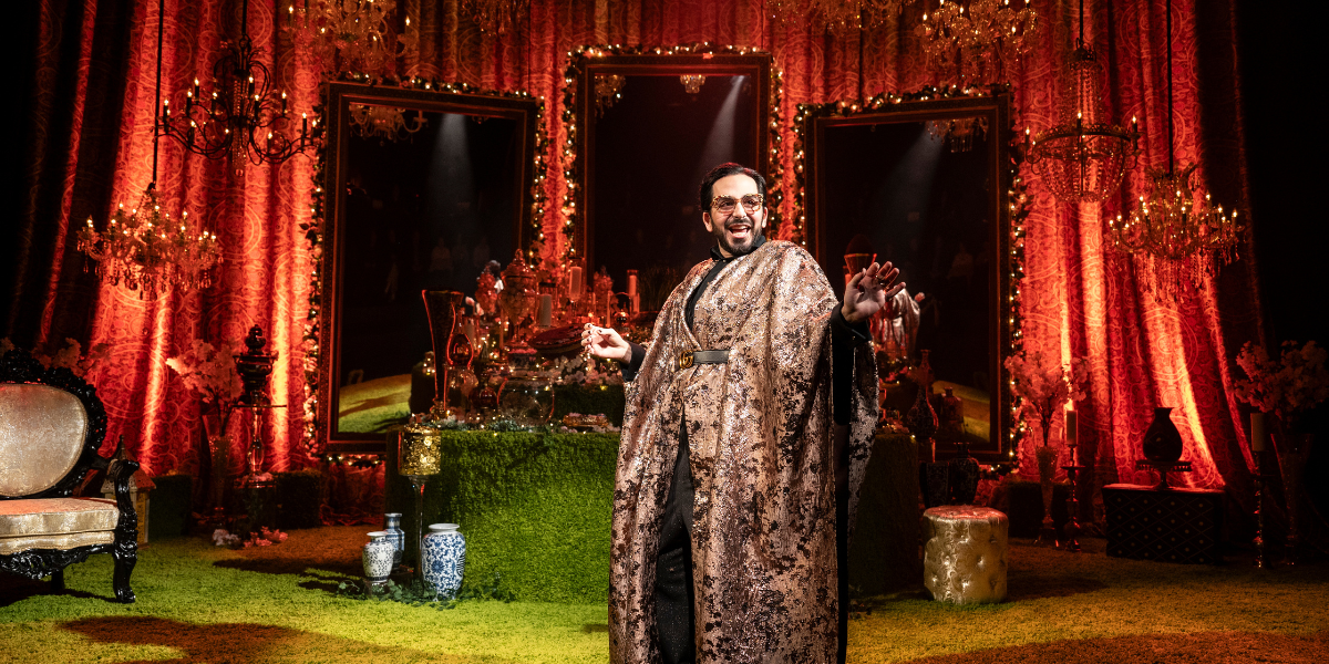 A person in a patterned robe standing in a richly
decorated room with red drapes, chandeliers, and mirrors.