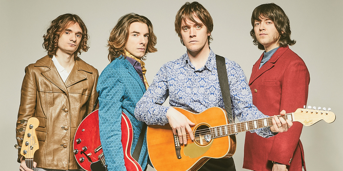 4 men staring seriously at camera posed in colorful 60's jackets holding instruments