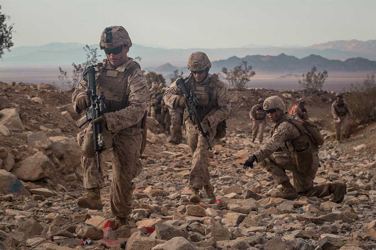 Group of service members walk through rocky terrain. Group of service members walk through rocky terrain.