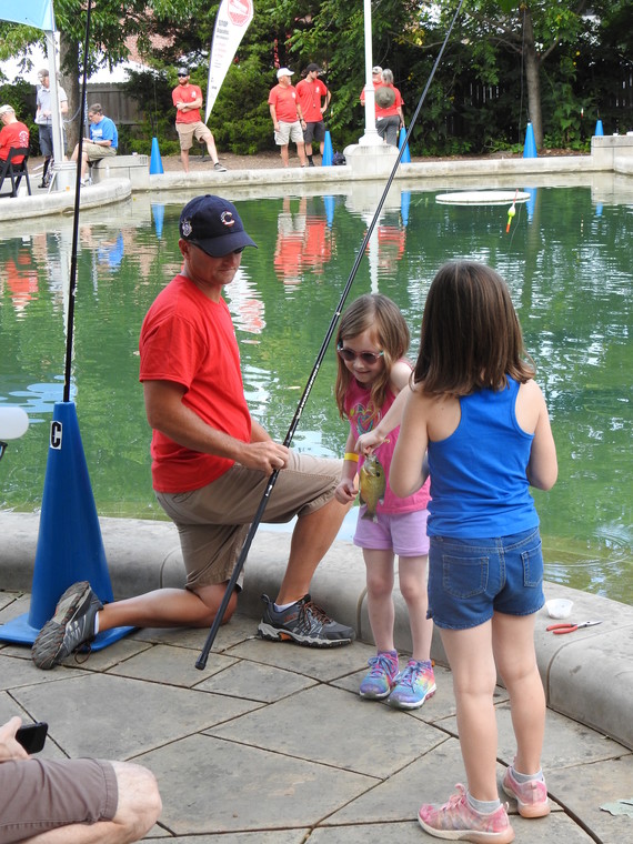 A man teaching two young girls to fish.