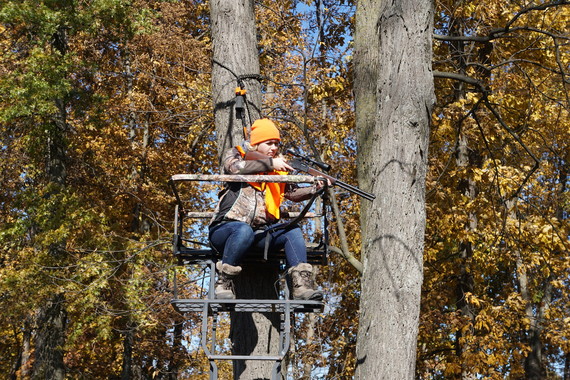A woman hunting from a tree stand in the forest.