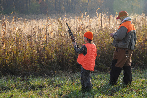 A youth hunter holding a gun beside their guardian outdoors.