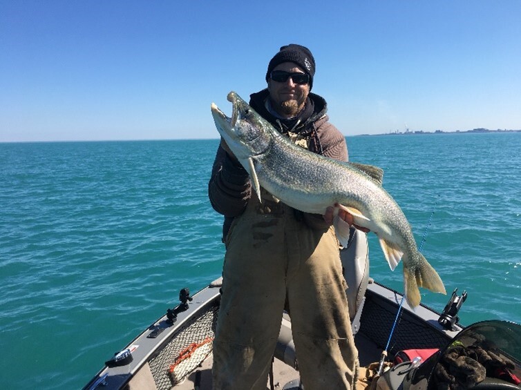 A man holding a large lake trout on a boat.