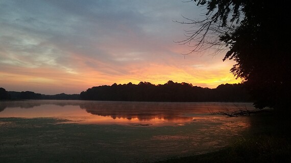 A sunset over a lake with trees in the background.