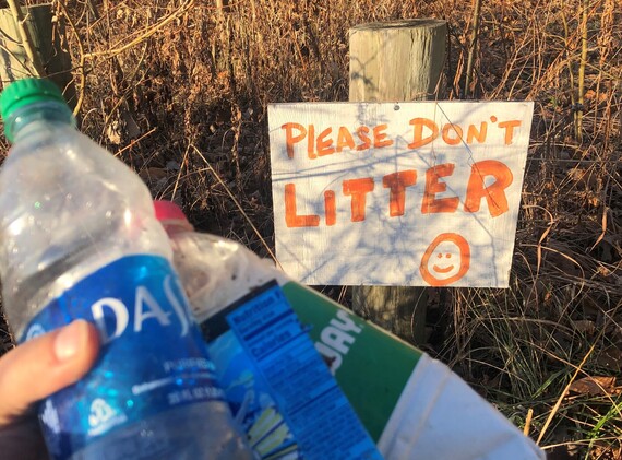 A “Please don’t litter” sign behind a hand holding plastic bottles.