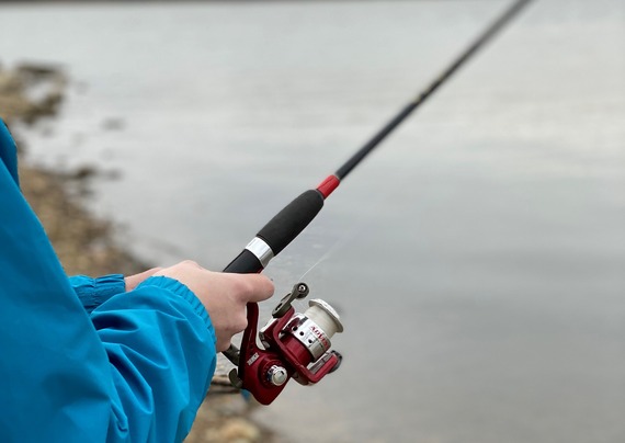 Two hands holding a fishing reel by the shoreline.