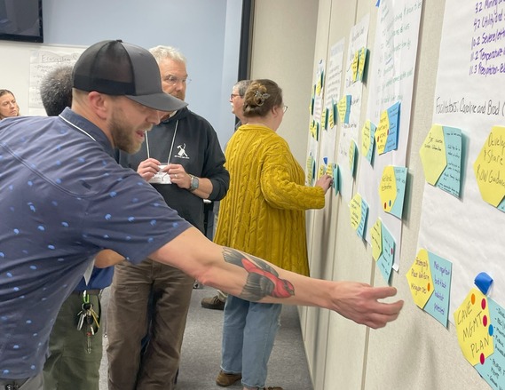 A man with a tattoo of a scarlet tanager on his arm placing a sticker on a piece of construction paper.