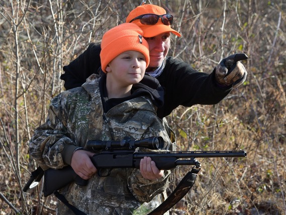 A young boy hunting with an older man.