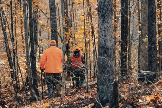 Two men wearing hunter orange and hunting in the woods.