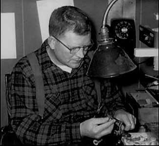 A historic photo shows Clarence Roberts tying flies.