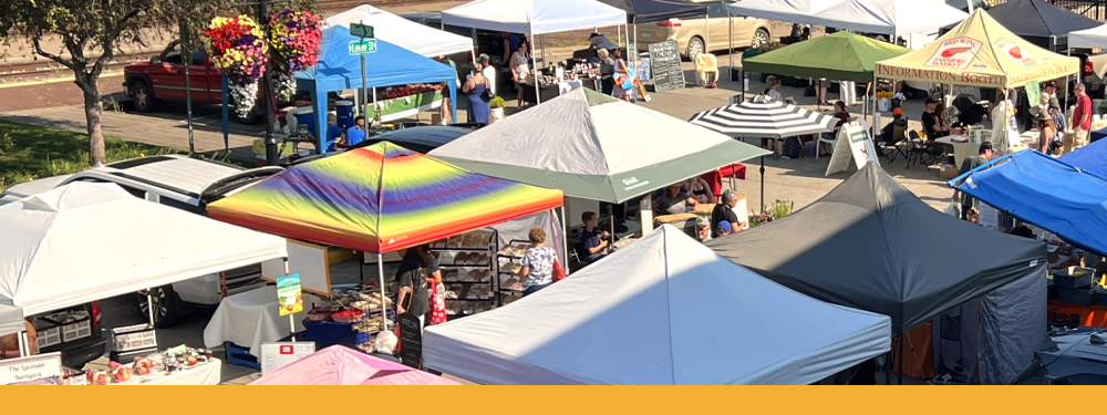 aerial view of white, black, blue, green, and rainbow pop-up tents with vegetables, fruit, and flowers peeking out from under