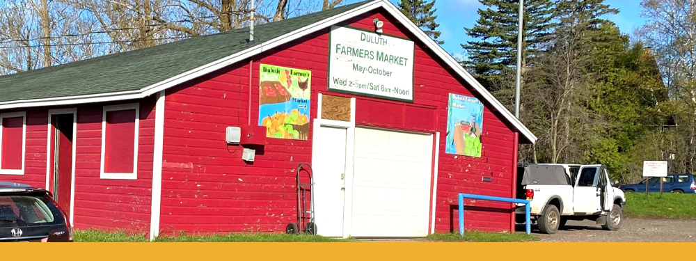 a bright red barn with sign reading, "DULUTH FARMERS MARKET" Signs hang on the barn showing chickens, pumpkins, and tomatoes.