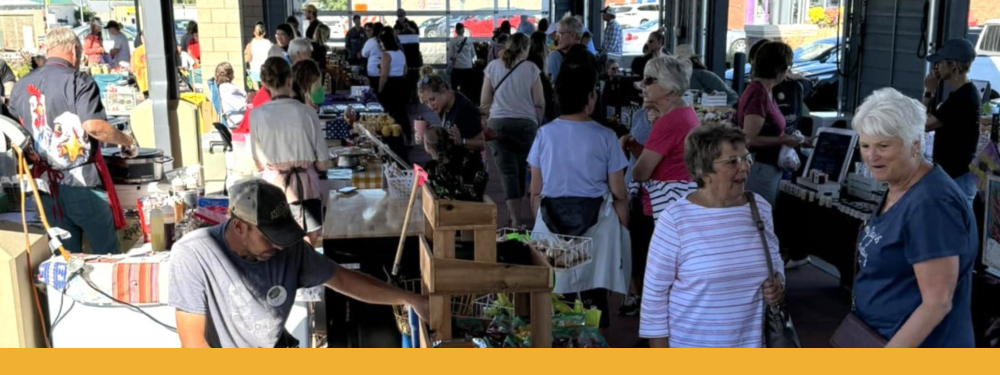 a busy market snapshot where people are viewing vegetables, honey, and more.