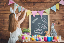 Child putting up Easter bunting in front of row of Easter eggs