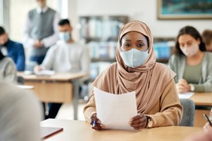 Black muslim female student at desk in mask