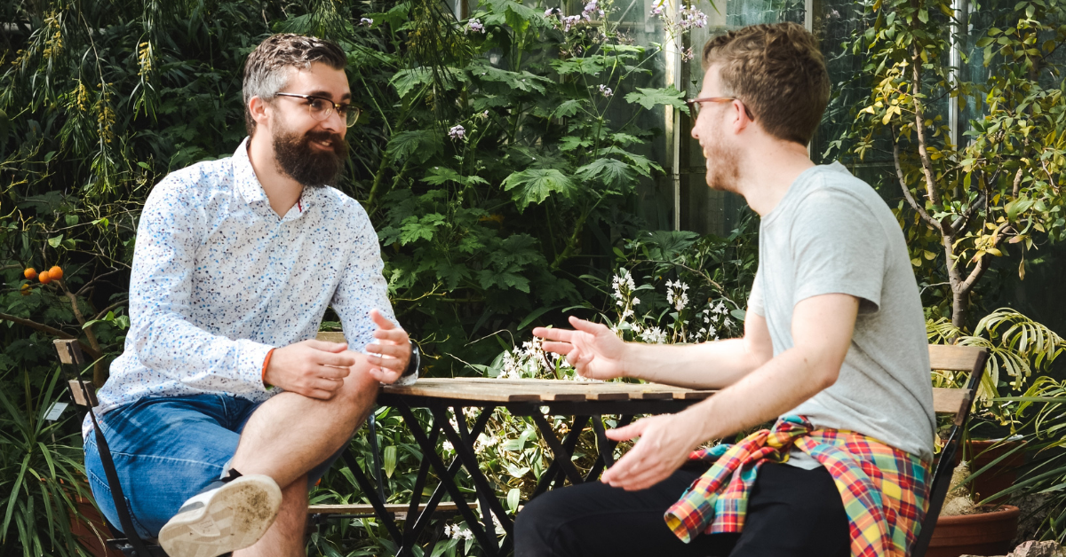 Two men talking at a sunny outdoor cafe table