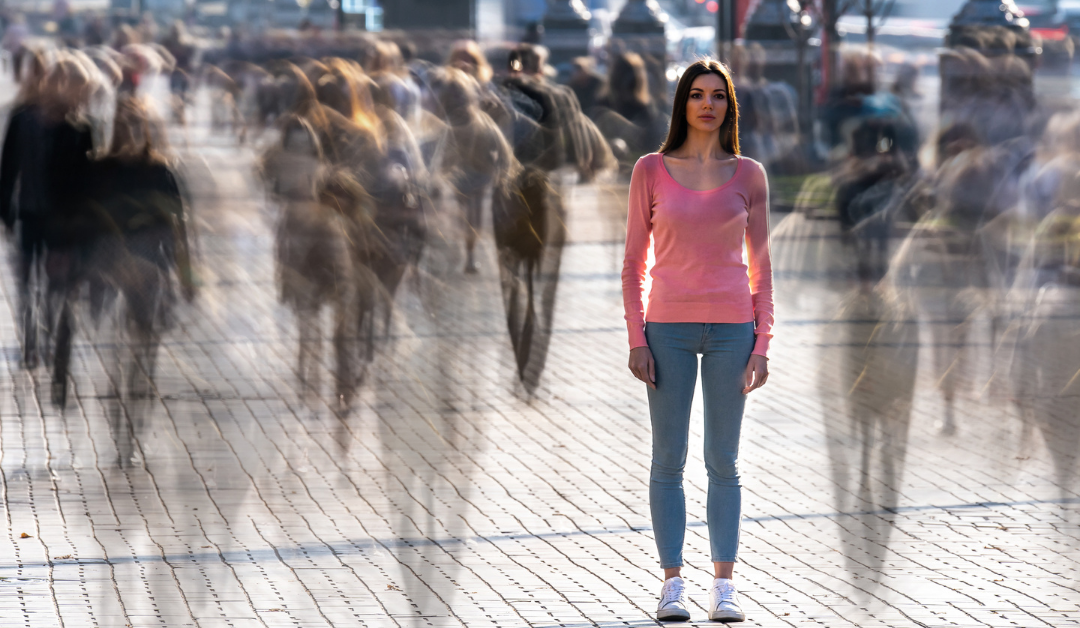 A woman standing on a sidewalk as the images of moving people swirl around her