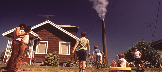 Strong laws and government agencies have measurably improved public health. In this 1972 photo, children play while a smelter in Tacoma, Washington, spews arsenic and lead residue. (Gene Daniels / EPA / National Archives)