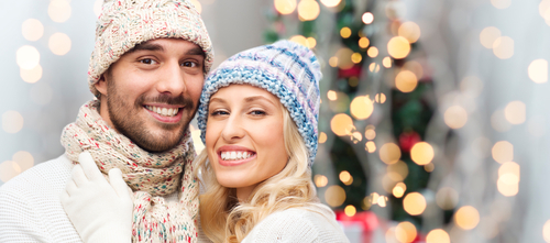winter_ fashion_ couple_ christmas and people concept - smiling man and woman in hats and scarf hugging over holidays lights background