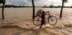 A Villager in Burichang area of eastern Comilla district struggles to cross potholes with his bicycle 15 July 1999 as gushing flood waters from the swelling Gumti river inundated the major Comilla-Sylhet highway.  Floods this week have left thousands of villagers homeless. AFP PHOTO (Photo by MUFTY MUNIR / AFP)