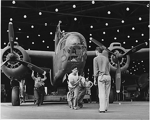 Black and white photograph of assembly line workers pulling an airplane out of the plant.
