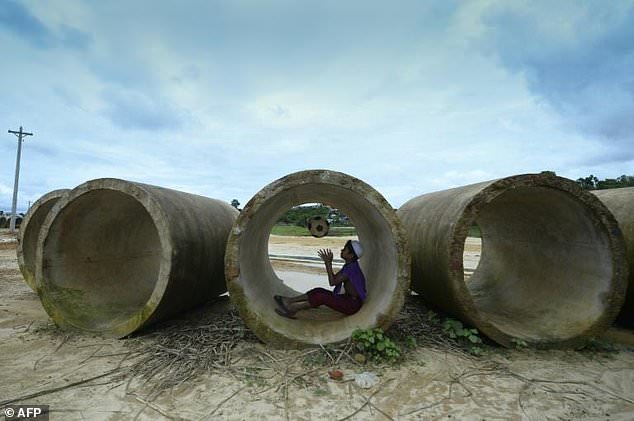 A Rohingya child plays with a football inside a sewage pipe at a refugee camp