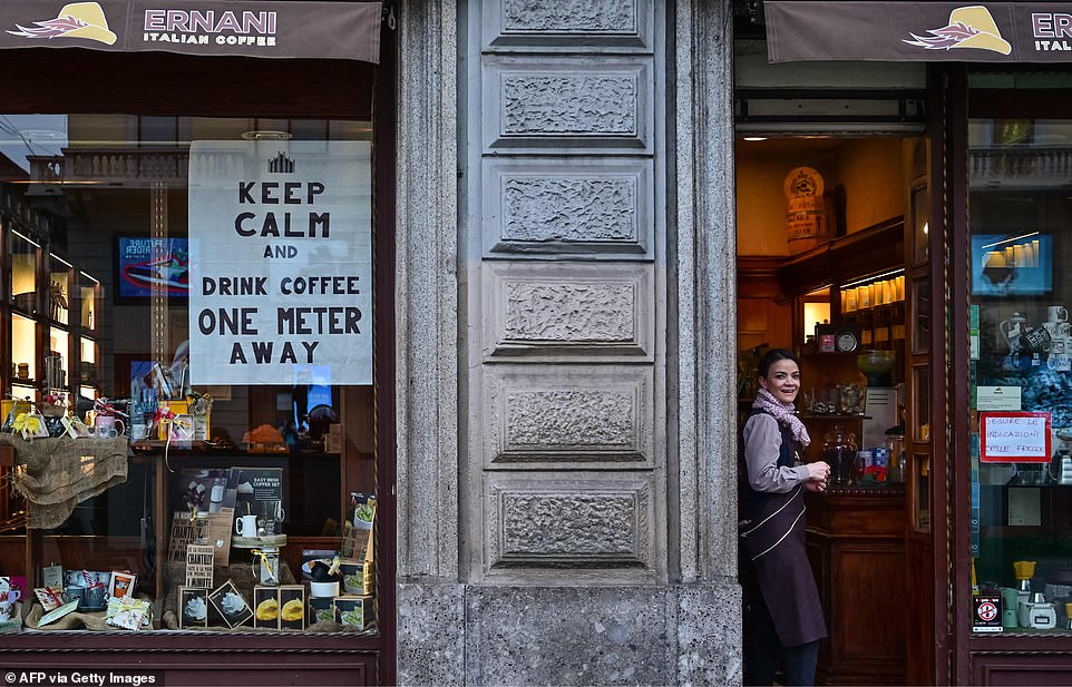 A waitress in Milan looks on by a sign advising clients to keep their distance from each other, under Italy's new quarantine rules