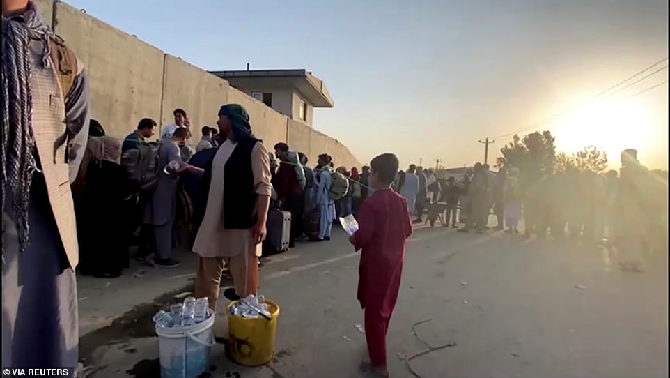 A man instructs people to queue as they stand with their belongings outside Kabul airport, Afghanistan