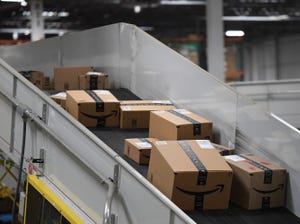 A series of different sized Amazon packages sit on a downwards-sloping conveyer belt with high walls.