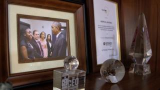 A desk with awards and a picture of Peju with President Obama