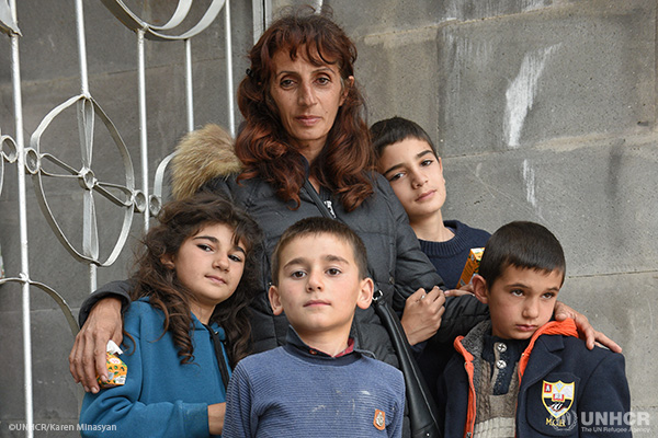 A refugee mother, standing with her arms around her four young children