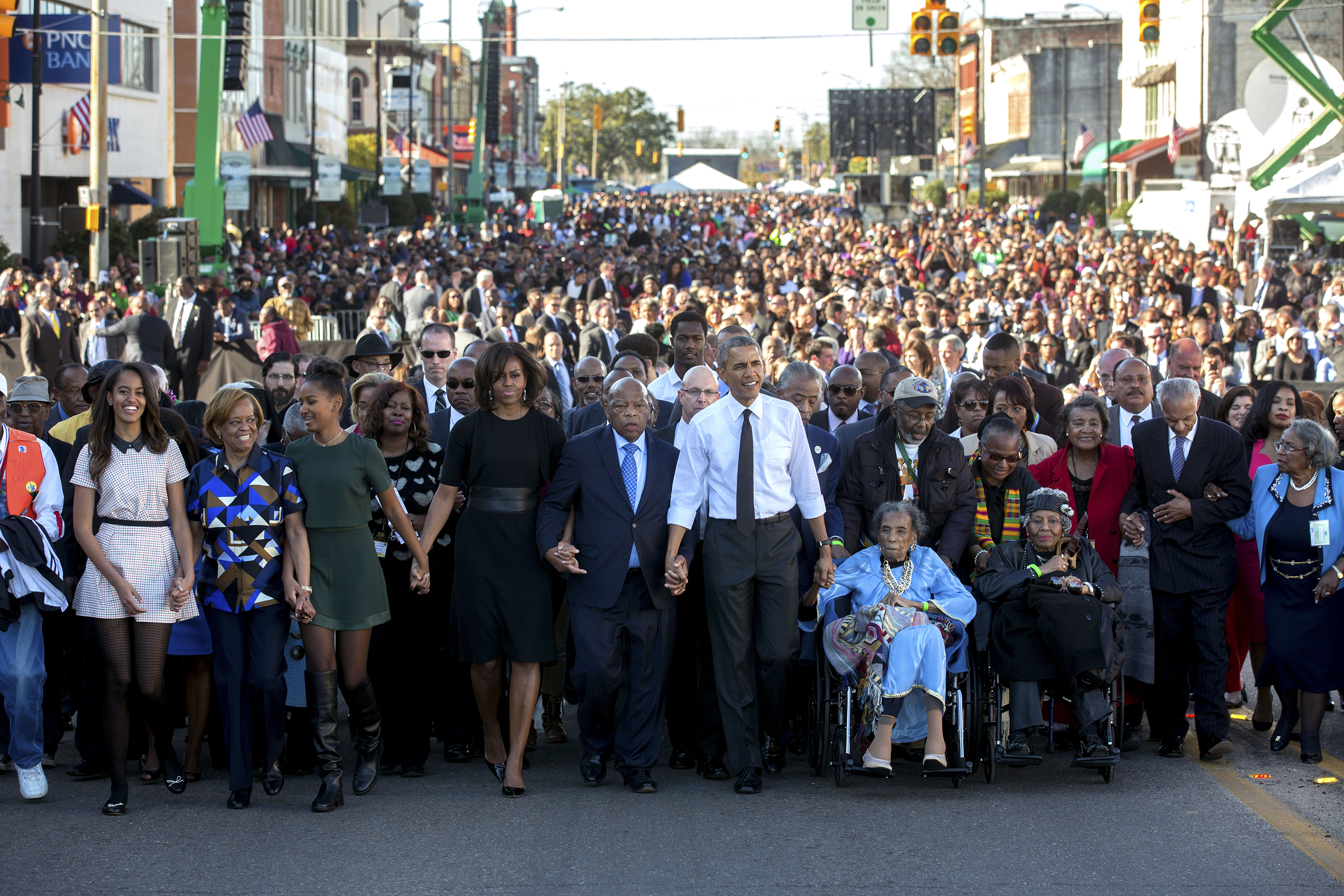 President and Mrs. Obama march holding hands down a street with a large crowd of people