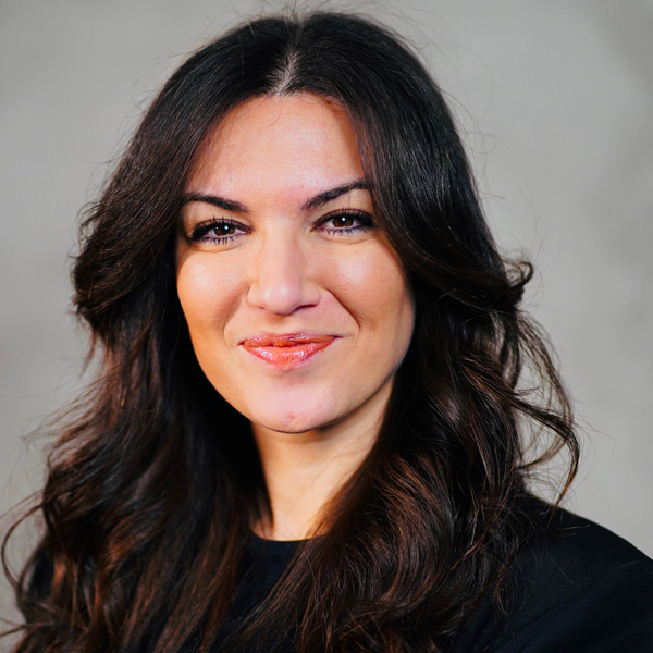 Ornella Cosomati, a woman with a light skin tone and long black hair, smiles at the camera. She has a closed lip smile and is wearing a black blazer.